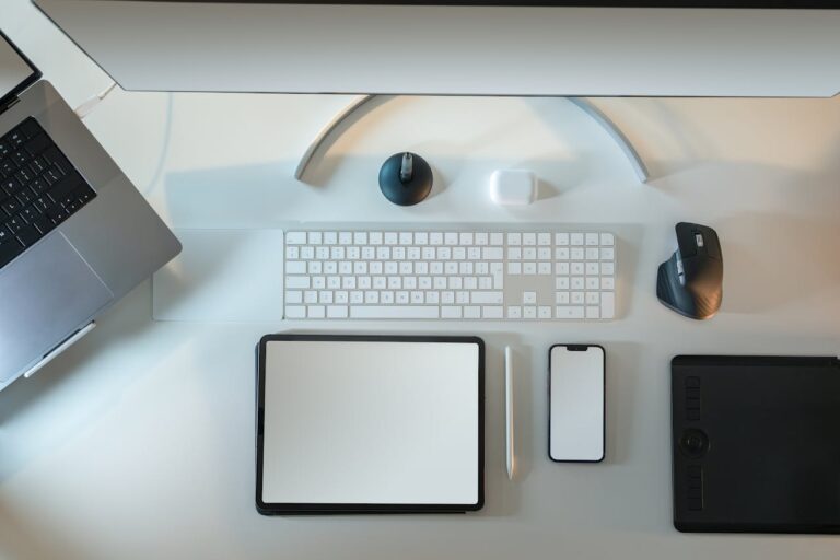 Top view of modern tech workspace featuring laptop, tablet, smartphone, and accessories.